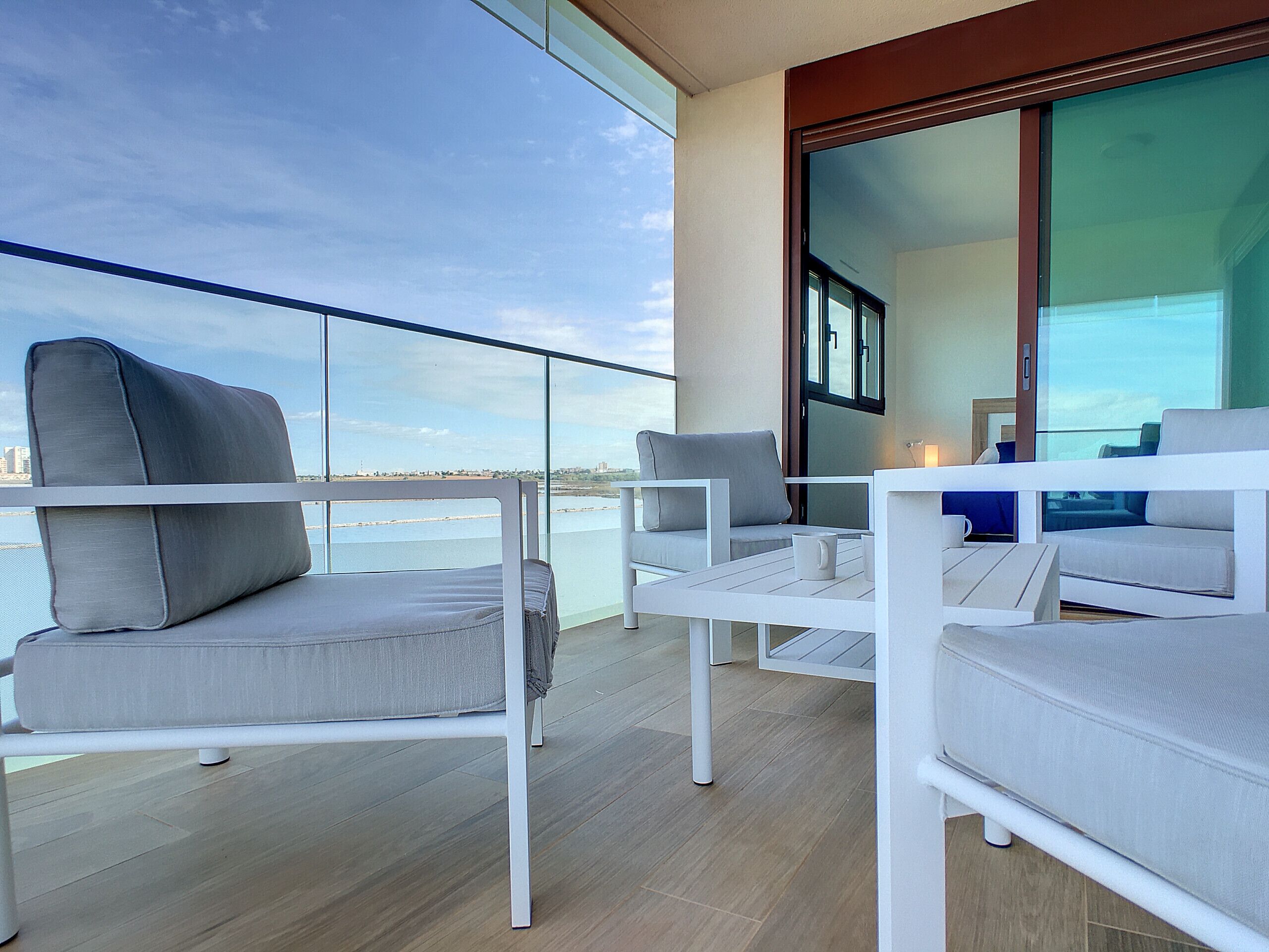 Un balcone con mobili bianchi, tra cui divani e poltrone, con vista su un corpo d'acqua.