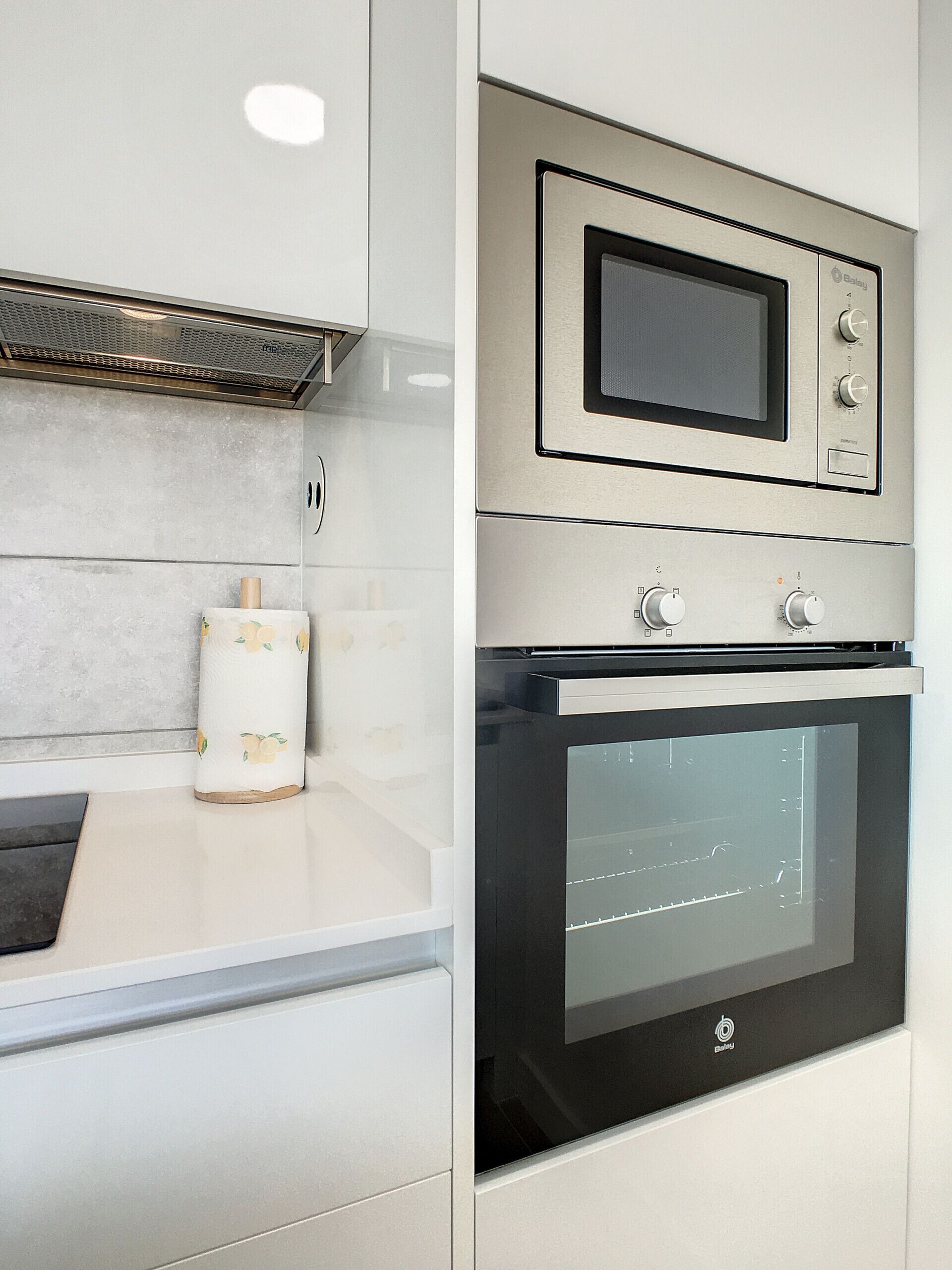 A modern kitchen with a built-in oven and microwave, a stainless steel range hood, and a white countertop.