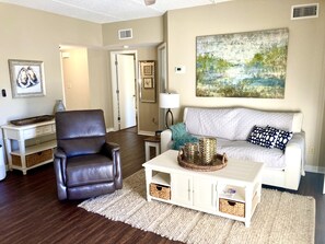 Ein Wohnzimmer mit braunem Ledersessel, weißem Sofa, weißem Couchtisch und einem Gemälde an der Wand.