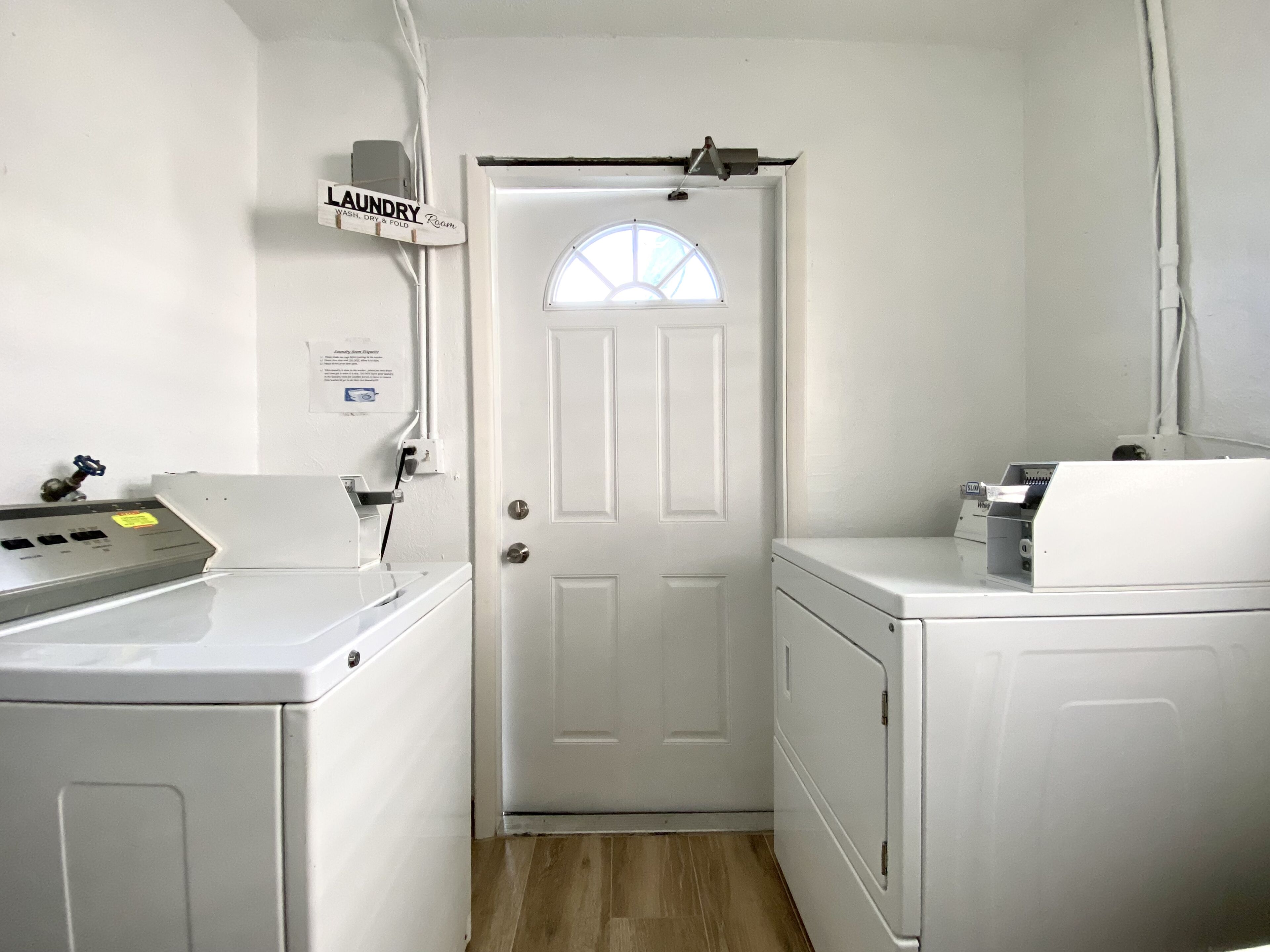 A laundry room with a white door, two washing machines, and a control panel.