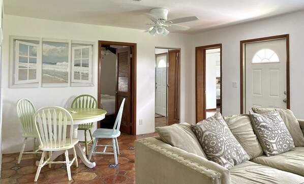 Una habitación con una mesa de comedor y sillas, un sofá con cojines estampados y un ventilador de techo.