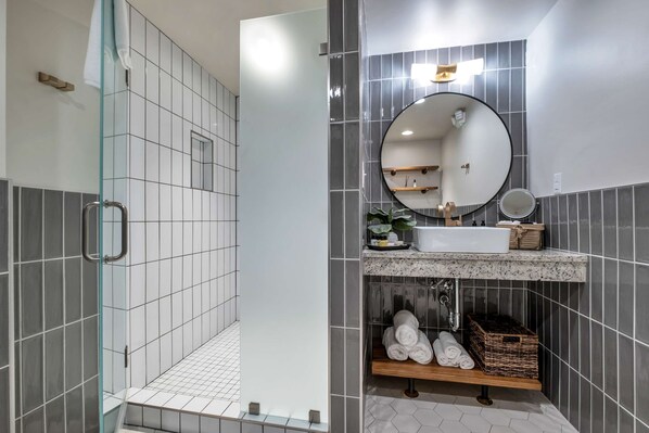 A modern bathroom with a glass shower enclosure, a round mirror, a sink with a marble countertop, and neatly folded towels.