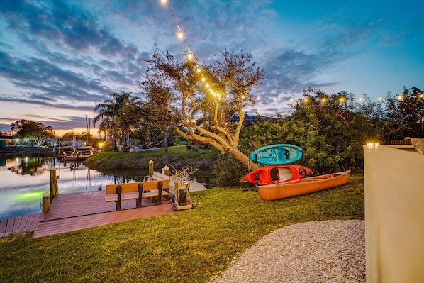 A dock with kayaks, a wooden bench, and a tree with string lights.
