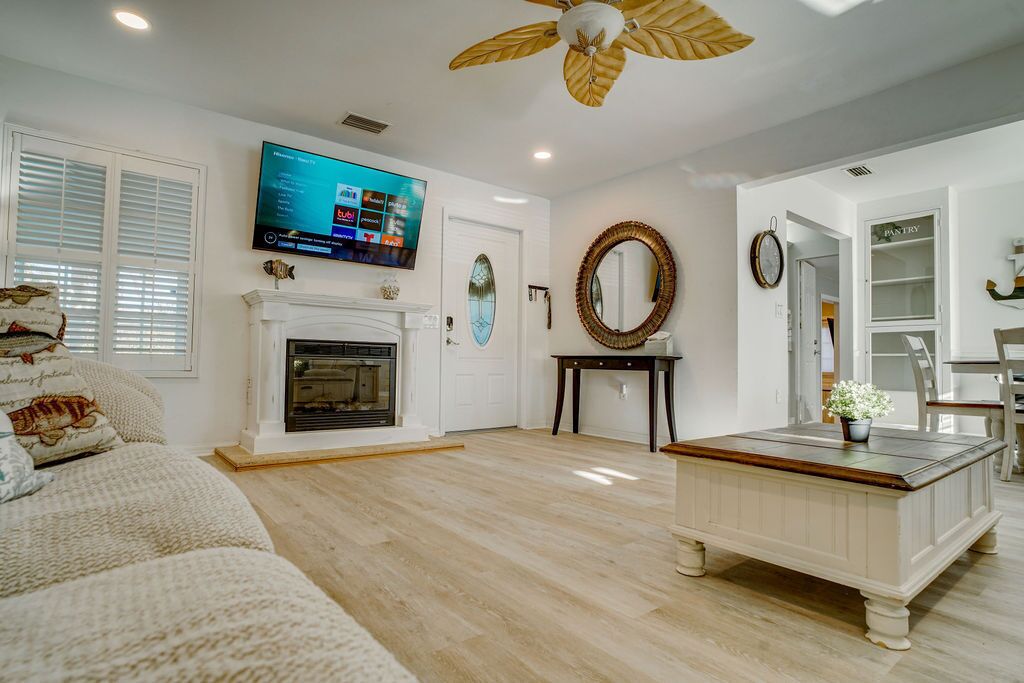 A living room with a fireplace, a television mounted above it, a ceiling fan, and a dining area with a chair and table.