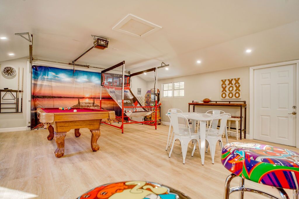 A room with a pool table, a hammock, and a dining area with white plastic chairs.