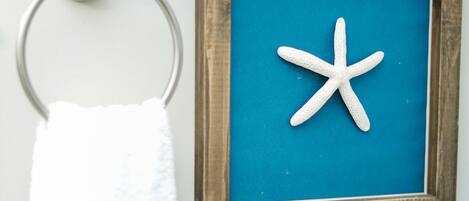 A bathroom with a white towel hanging on a metal ring, a framed picture of a starfish on the wall, a small potted plant, and a tissue box.