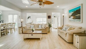 A spacious living room with a beige sofa, a coffee table, and a ceiling fan. There is a dining area with wooden chairs and a table. - Manatee Cove: Private Oasis with Wildlife, Hot Tub & Fun Game Room! (Bradenton)