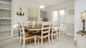 A dining area with a wooden table and white chairs, a chandelier, and a sign that says "COFFEE". - Manatee Cove: Private Oasis with Wildlife, Hot Tub & Fun Game Room! (Bradenton)