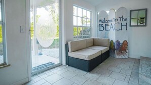 A modern interior with a sliding glass door leading to a patio, a beige sofa, and a wall with a 'Welcome to the Beach' sign. - Manatee Cove: Private Oasis with Wildlife, Hot Tub & Fun Game Room! (Bradenton)