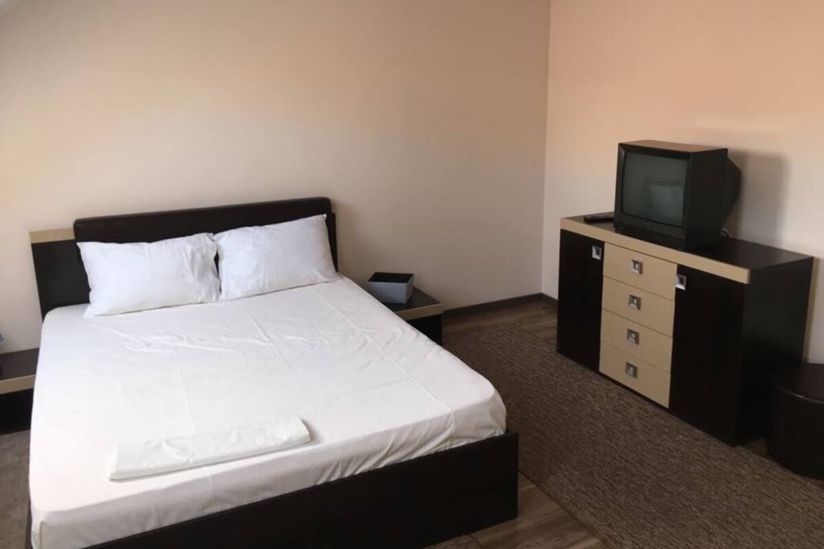 Una habitación de hotel con cama, televisión en un mueble y una pequeña mesa.