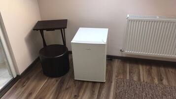 A compact room with a small refrigerator, a black trash bin, a table, and a radiator.