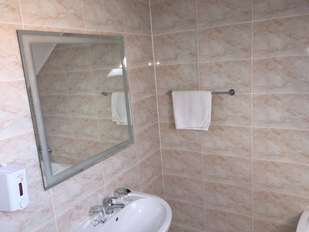 A bathroom with a marble-tiled wall, a sink with a mirror, and a towel rack.