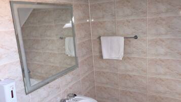 A bathroom with a marble-tiled wall, a sink with a mirror, and a towel rack.