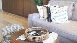 A living room with a grey sofa, a round wooden coffee table, and a patterned ottoman.