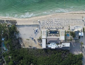 An aerial view of a coastal hotel with a beach area, multiple swimming pools, and a parking lot.