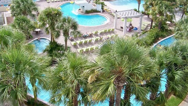 Ein Resort mit mehreren Schwimmbecken, umgeben von Palmen und Liegestühlen.