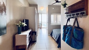 Ein Flur mit Fernseher, Schreibtisch, Pflanze, Bett und einem an der Wand befestigten Gepäckträger.