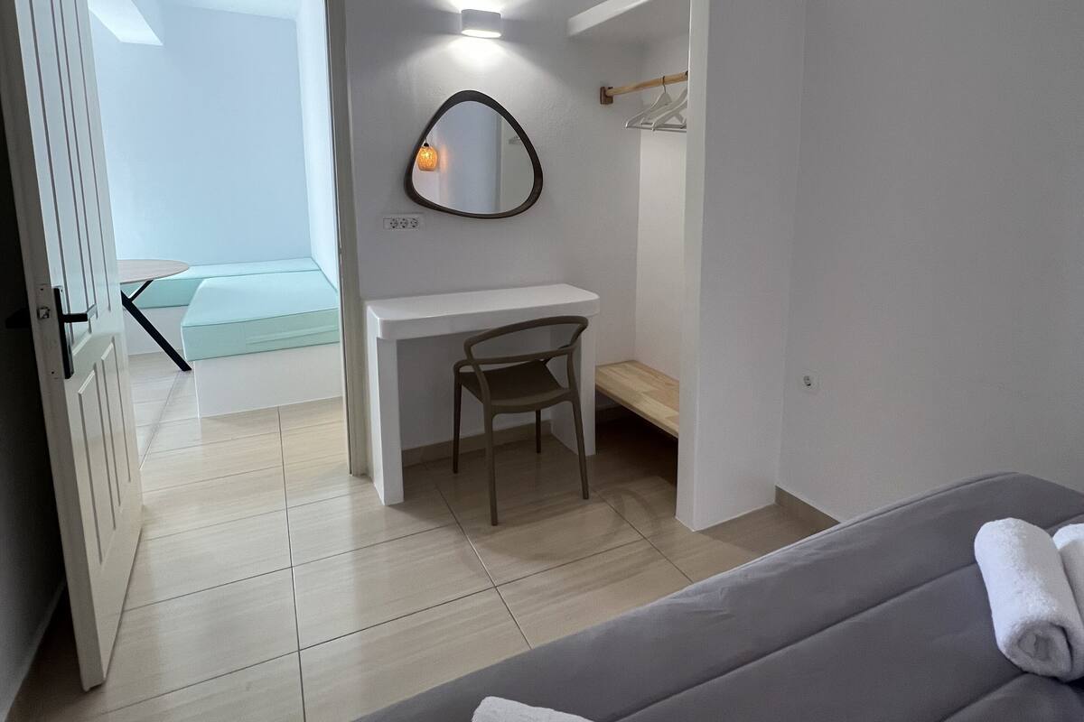 Een moderne slaapkamer met een bed, een bureau en een stoel. Er hangt een spiegel aan de muur en een deur die leidt naar een andere kamer.