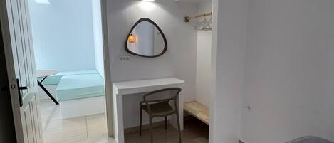 Un dormitorio moderno con una cama, un escritorio y una silla. Hay un espejo en la pared y una puerta que da a otra habitación.