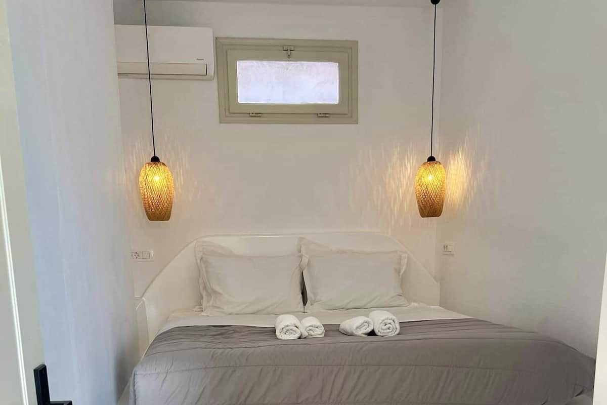 Een slaapkamer met een bed, twee bedlampen, een raam en een klein badkamertje.