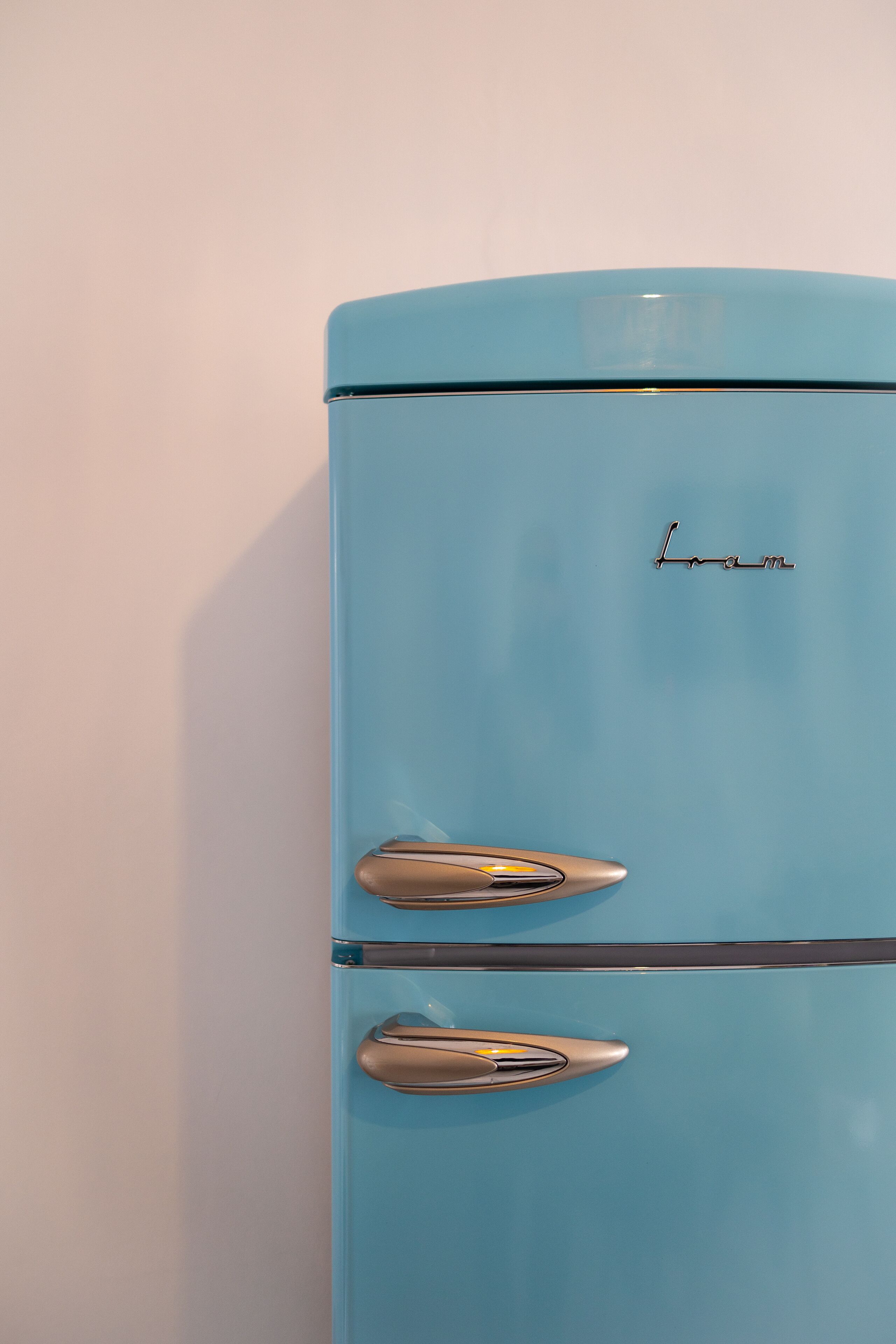A light blue vintage refrigerator with the brand name "Lom" on the top.