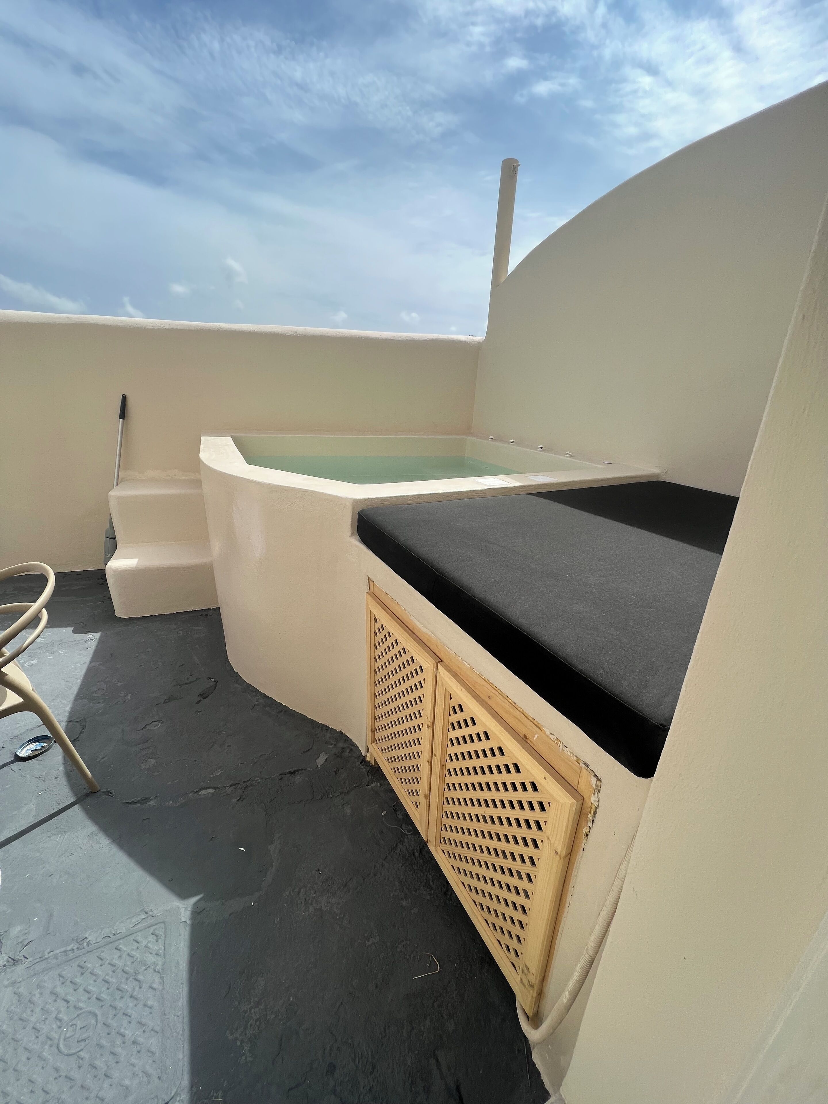 Une terrasse sur le toit avec un jacuzzi, un petit escalier menant à celui-ci et une chaise en métal.