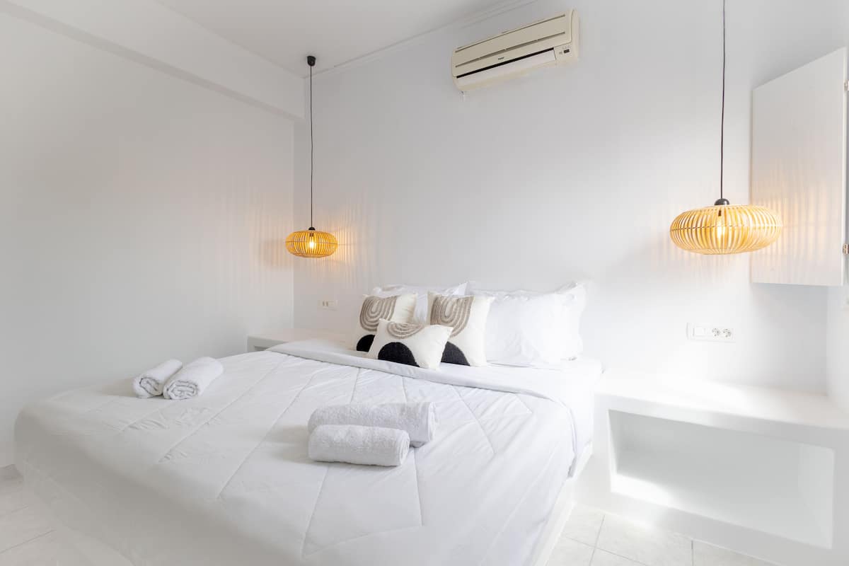 Een witte slaapkamer met een bed, twee bedlampen, een nachtkastje en een airconditioner.