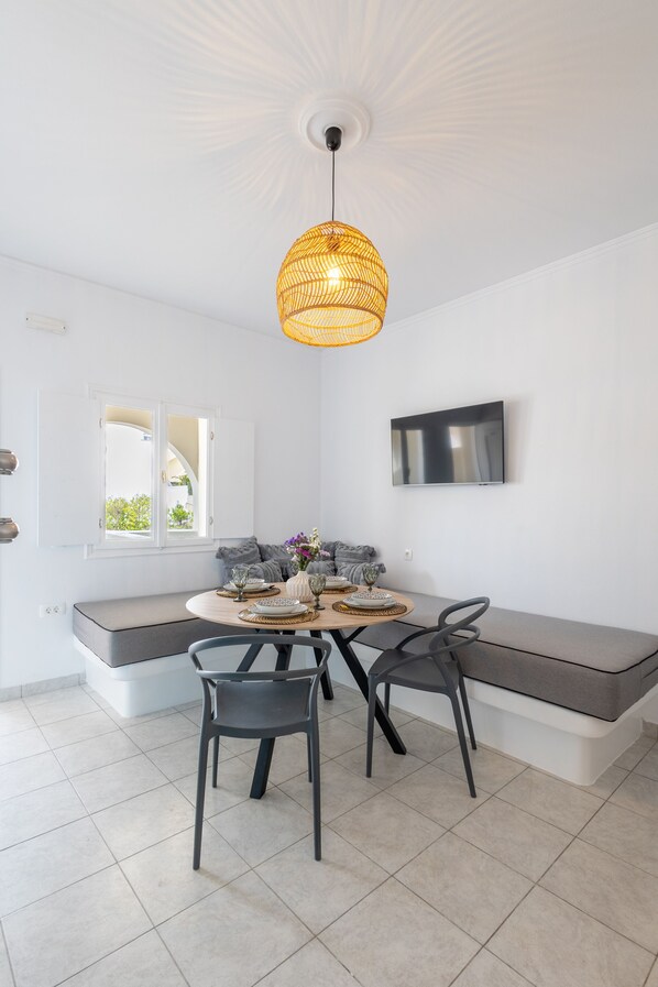 A modern living room with a round table, two chairs, a sofa, and a TV mounted on the wall.