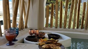 Un comedor con vista a la piscina, pilares de madera y una mesa con comida y bebidas.