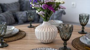Una mesa de comedor dispuesta con platos, cubiertos y copas, junto a un jarrón con flores.