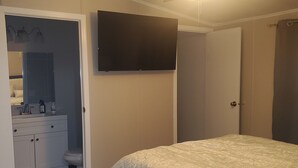Makuuhuoneessa on sänky, kattotuuletin, seinälle asennettu televisio ja ovi, joka johtaa toiseen huoneeseen.