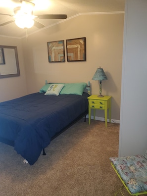 Un dormitorio con una cama, una mesita de noche, una lámpara y dos cuadros colgados en la pared.