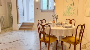 Un comedor con suelo de mármol, sillas de madera, mantel blanco y un mapa en la pared.