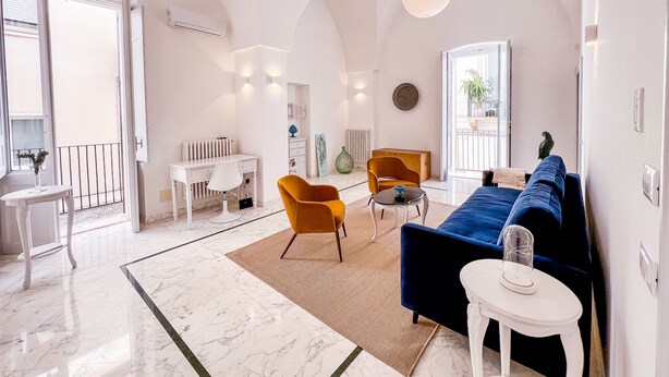 Amplia sala de estar con piso de mármol, un sofá azul, un sillón amarillo y un escritorio blanco.