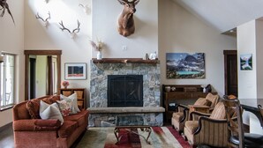 A spacious living room with a stone fireplace, wooden flooring, and a ceiling fan. - Private estate on 8 acres with lake access (Whitefish)