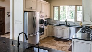 A modern kitchen with white cabinets, stainless steel appliances, a black countertop, and a window providing natural light. - Private estate on 8 acres with lake access (Whitefish)