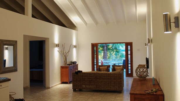 Amplia sala de estar con techo alto, sofá de mimbre, mesa de centro de madera y vistas a un área exterior a través de una puerta de vidrio.
