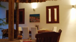 Una mesa de comedor de madera con sillas, techo de paja y luces colgantes.