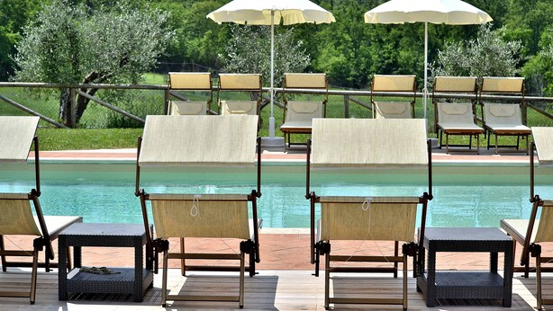 Ein Poolbereich mit Liegestühlen und Sonnenschirmen, mit Blick auf einen Pool und eine malerische Landschaft.