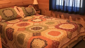 Ein gemütliches Zimmer mit Holzvertäfelung, einer gesteppten Bettdecke, einem gerahmten Bild an der Wand und einem Fenster mit Vorhängen.