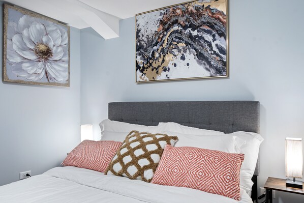 A modern bedroom with a grey headboard, white bedding, and patterned pillows.