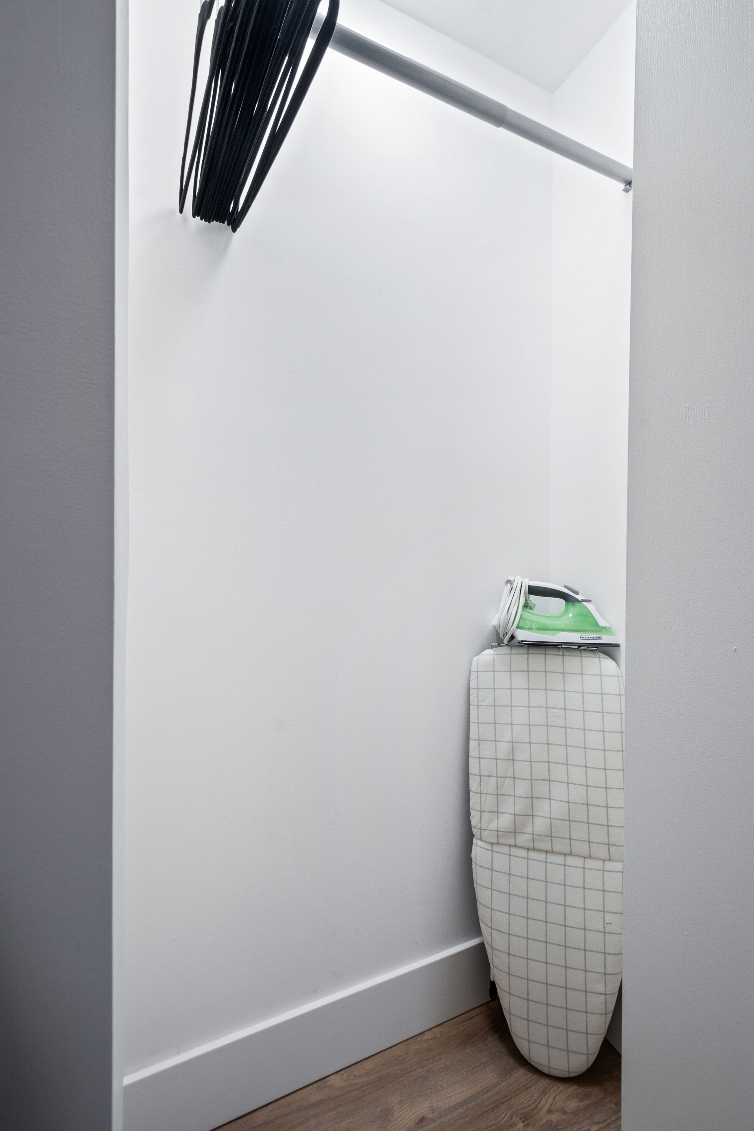 A bathroom with a white wall, a wooden floor, and a green and white ironing board.