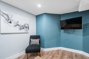 A room with a blue accent wall, a mounted TV, a black chair, and a white abstract painting.