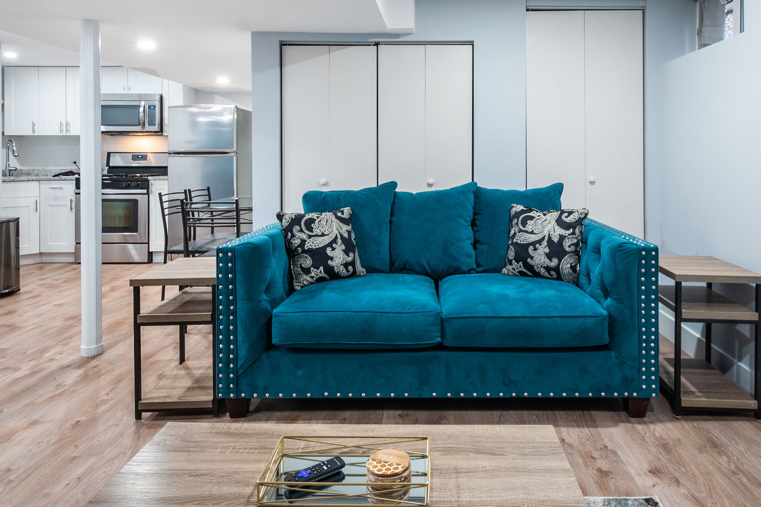 Un salon moderne avec un canapé de couleur turquoise, une table à manger et un coin cuisine à l’arrière-plan.