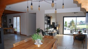 Un comedor amplio con una mesa y sillas de madera, una planta en maceta y vistas al exterior a través de un ventanal.