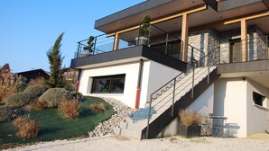 Una casa moderna de dos pisos con un balcón, una escalera y un pequeño jardín.