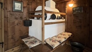 Interior d'una cabana de fusta amb un llit superposat, una taula petita i un cubell.