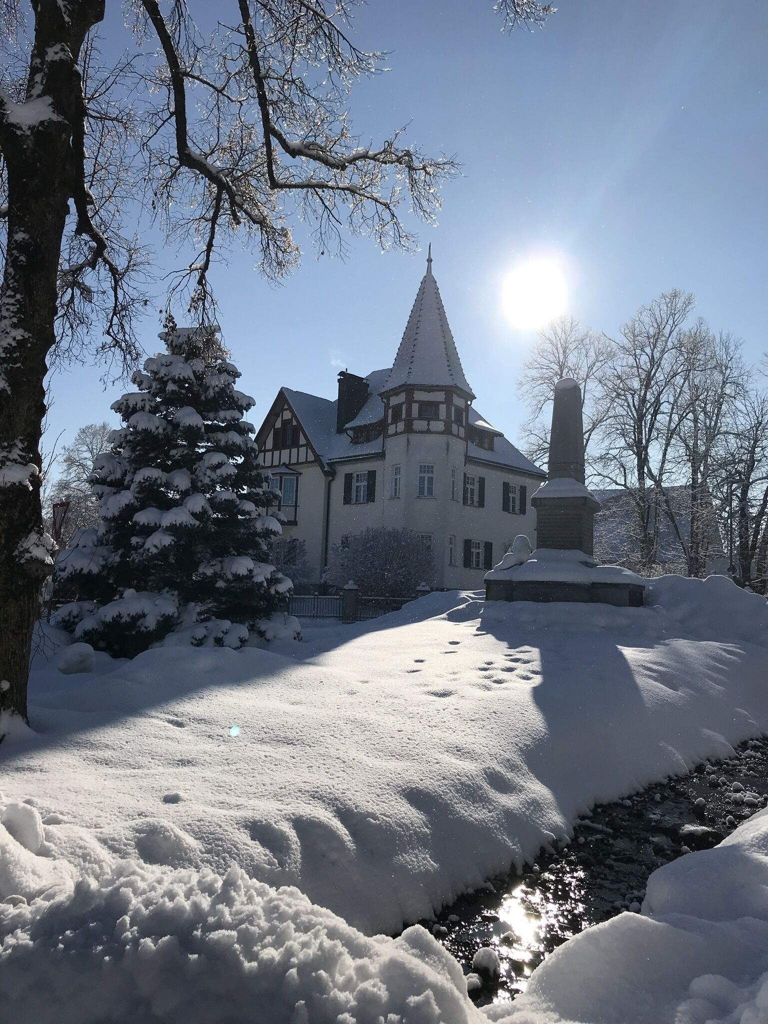A snow-covered building with a prominent tower, surrounded by trees and a snow-covered landscape.
