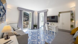 A modern hotel room with a large bed, a sofa, a desk, and a TV. The room has a view of a mountainous landscape through the window. - Casa Diodora, vicino al mare, in Costiera Amalfitana (Maiori)