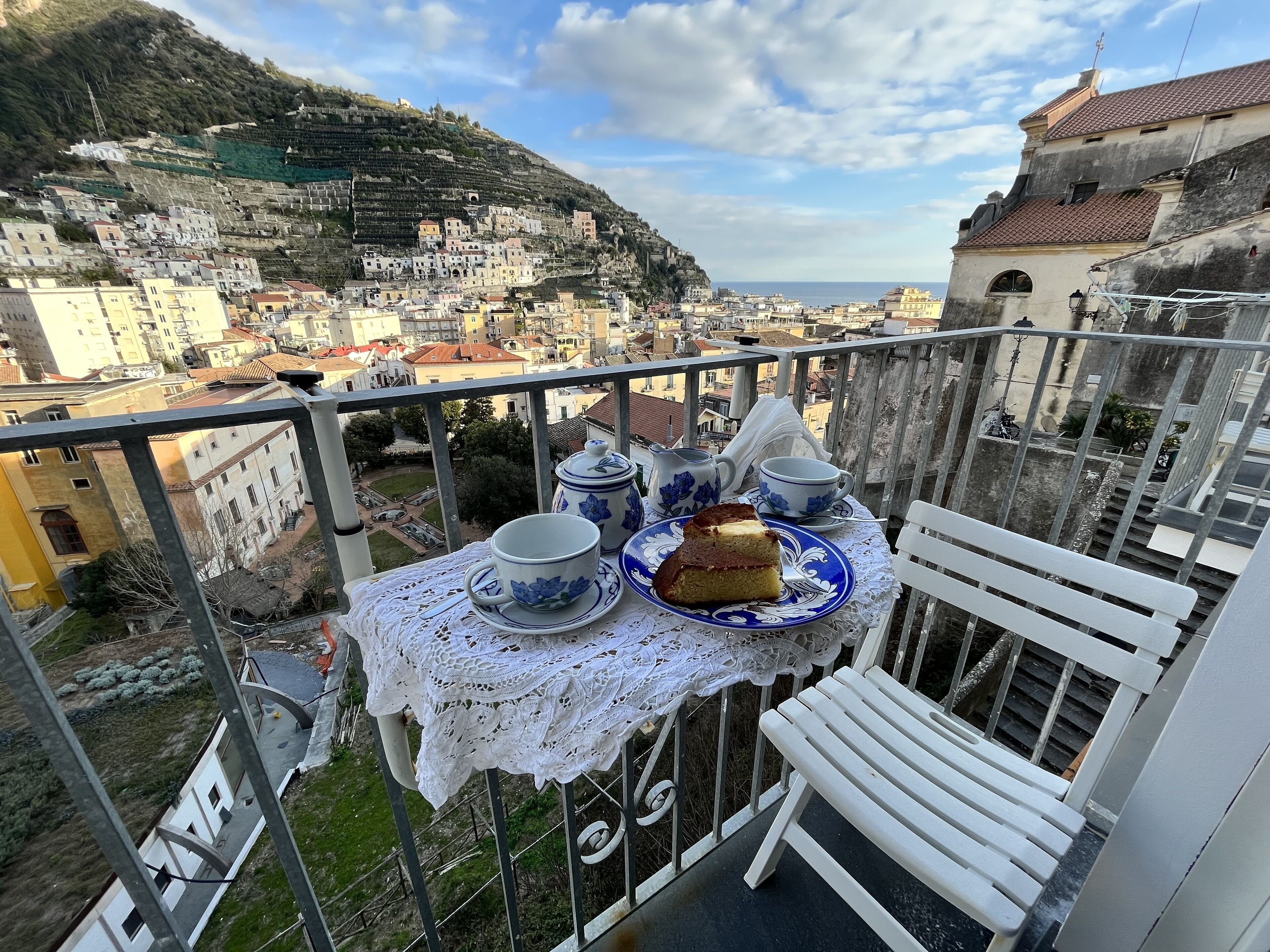 Un balcon avec une table dressée pour le thé, donnant sur une ville située sur une colline.
